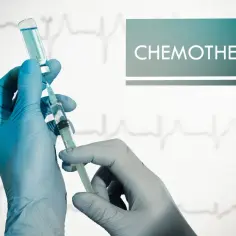 Rękawiczki medyczne przygotowują zastrzyk do chemioterapii. Na tle widać wykres EKG.