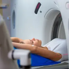 Kobieta leży na łóżku tomografu. Czy do tomografii trzeba się rozbierać? Zazwyczaj nie, wystarczy zdjąć metalowe przedmioty.