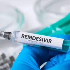 Strzykawka z płynem **remdesivir** w rękawiczce medycznej, gotowa do podania.