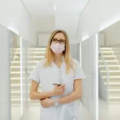 Kobieta w białym kitlu i różowej masce, z zeszytem i długopisem, gotowa do pracy. Cito!