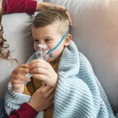 Chłopiec z maską nebulizatora, otulony kocem, czuje się jakby dopadła go klątwa Ondyny. Mama czule go głaszcze.
