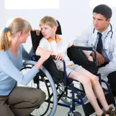 Chłopiec z dystrofią mięśniową Duchenne'a w wózku inwalidzkim rozmawia z matką i lekarzem.