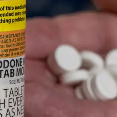 Pigułki Oxycodone 5/325 mg w dłoni, obok butelki z ostrzeżeniami.