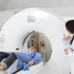 Pacjentka leży w skanerze CT, przygotowując się do angiografii głowy. Lekarka nadzoruje badanie.