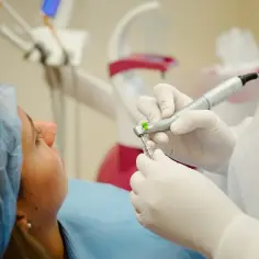 Dentysta zakłada wypełnienie kompozytowe. Pacjentka w czepku leży na fotelu.