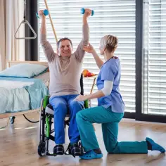 Starszy mężczyzna w wózku ćwiczy z hantlami pod okiem fizjoterapeutki. Rehabilitacja przynosi ulgę, a zwrot z ulgi rehabilitacyjnej 2280 może pomóc w dalszym leczeniu.