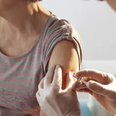 Osoba w rękawiczkach podaje zastrzyk w ramię starszej kobiety. Choć szczepionka Pfizer jest bezpieczna, niektórzy doświadczają skutków ubocznych.