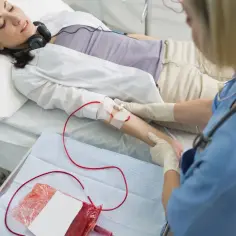 Kobieta leży w łóżku, słuchając muzyki przez słuchawki, podczas gdy pielęgniarka wykonuje transfuzję krwi.