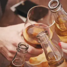 Ludzie wznoszą toast butelkami piwa i kieliszkiem z bursztynowym płynem. Pytanie: czy po szczepieniu można pić alkohol?