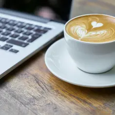Kawa latte z sercem na piance obok laptopa. Idealny moment na picie kawy po operacji zaćmy, by cieszyć się ostrością widzenia i smakiem.