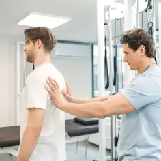 Fizjoterapeuta bada plecy pacjenta, oceniając jego stan przed rozpoczęciem rehabilitacji. Zastanawiasz się, ile zabiegów w sanatorium z NFZ czeka Cię po kontuzji?