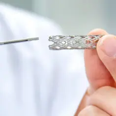 Dłoń trzyma metalowy stent, obok narzędzie medyczne. Badania nad tym, jak długo wytrzymują stenty, są kluczowe dla kardiologii.
