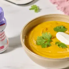 Odżywczy krem dyniowy z kleksem śmietany i kolendrą. Obok butelka Nutridrink Protein Omega 3, wspierająca leczenie. Pytanie: jakich witamin unikać przy nowotworach?