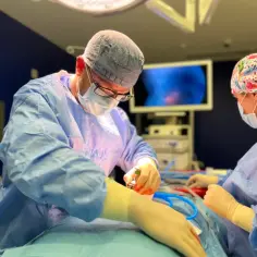 Chirurg wykonuje operację przepukliny, skupiony na precyzyjnym działaniu. W tle monitor pokazuje obraz z wnętrza ciała.
