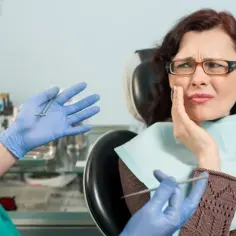 Kobieta z bólem zęba u dentysty. Lekarz w rękawiczkach pokazuje narzędzia, sugerując leczenie zatrucia zęba.
