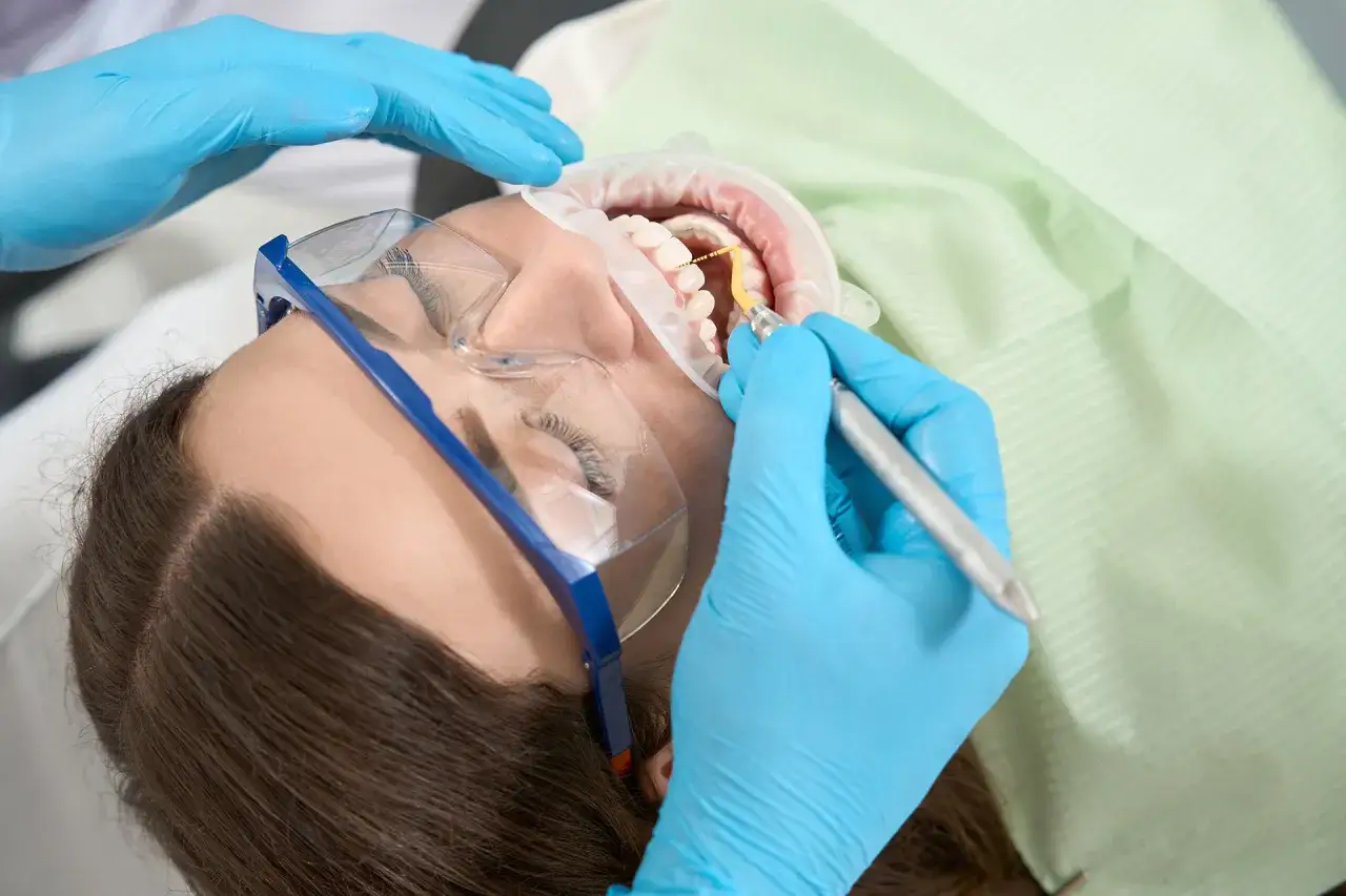 Dentysta wykonuje czyszczenie zębów pacjentki, używając specjalistycznego sprzętu.