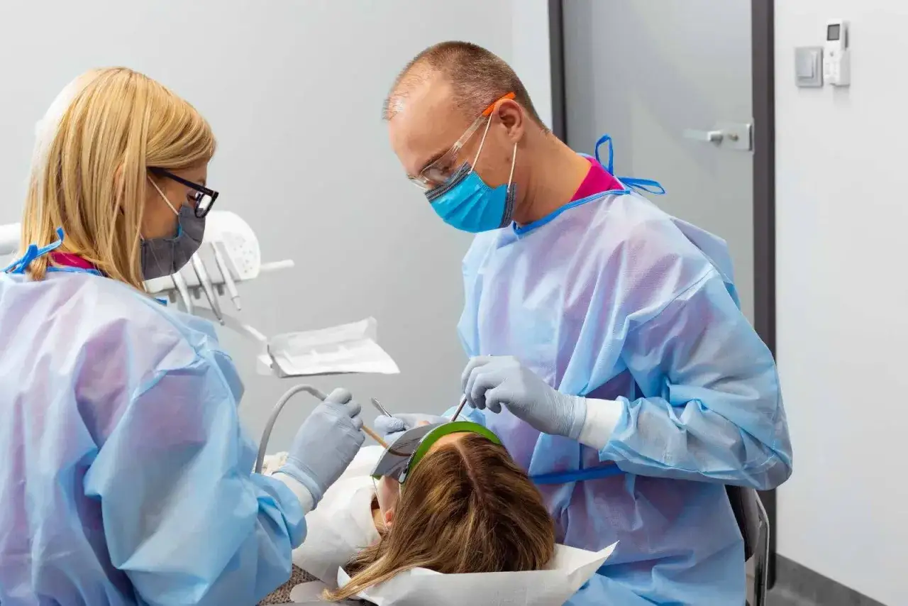 Dentysta i asystentka w fartuchach i maskach przygotowują się do wyrywania ósemki. Pacjentka leży na fotelu.