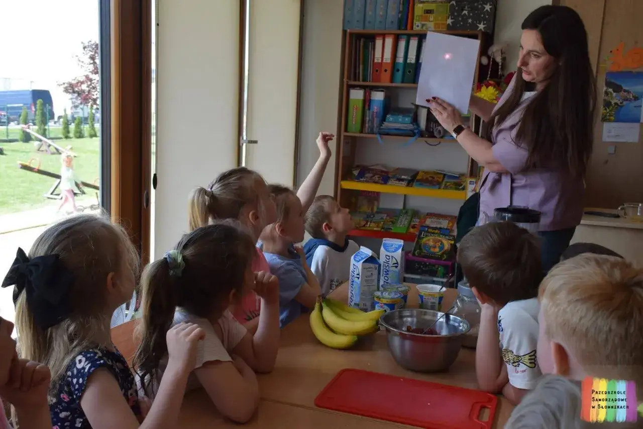 Nauczycielka pokazuje dzieciom eksperyment z laserem, omawiając edukacja zdrowotna tematy. Dzieci z zaciekawieniem obserwują.