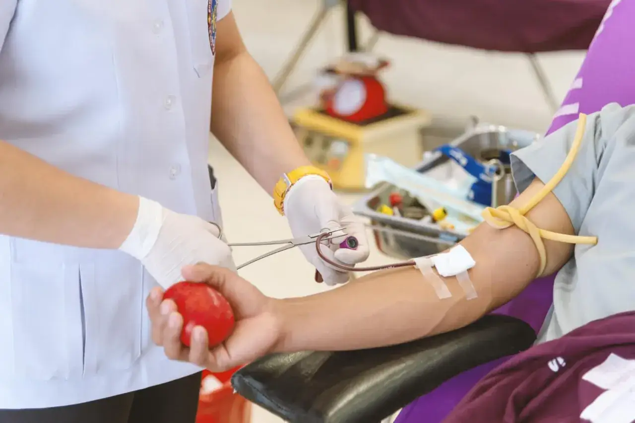 Pielęgniarka przygotowuje transfuzję krwi. Pacjent ściska czerwoną piłkę, podczas gdy pielęgniarka zakłada opaskę uciskową na jego ramię.