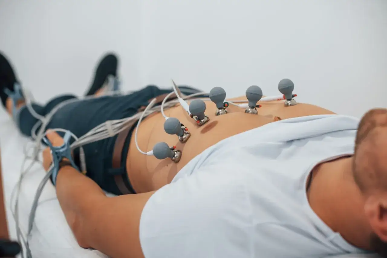 Pacjent leży z elektrodami EKG na klatce piersiowej. Badanie EKG jest szybkie i bezbolesne, a jego czas trwania zależy od rodzaju badania.