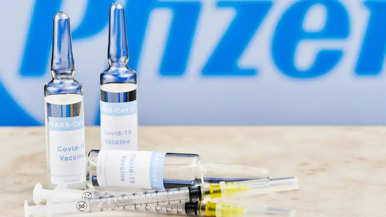 Szczepionki Pfizer Covid-19 w ampułkach i strzykawkach na tle logo firmy.