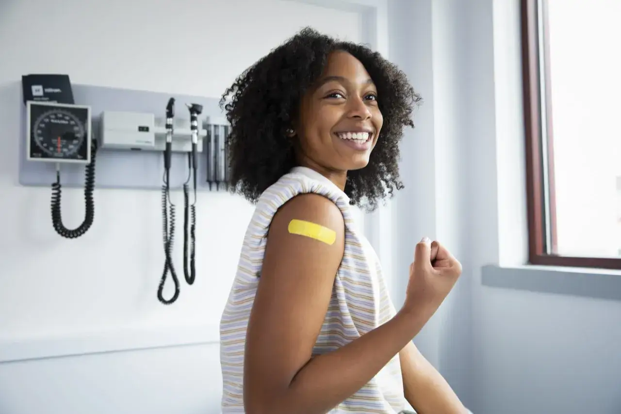 Uśmiechnięta dziewczyna z plastrem po szczepieniu HPV. Choć szczepienie hpv skutki uboczne są rzadkie, warto pamiętać o profilaktyce.
