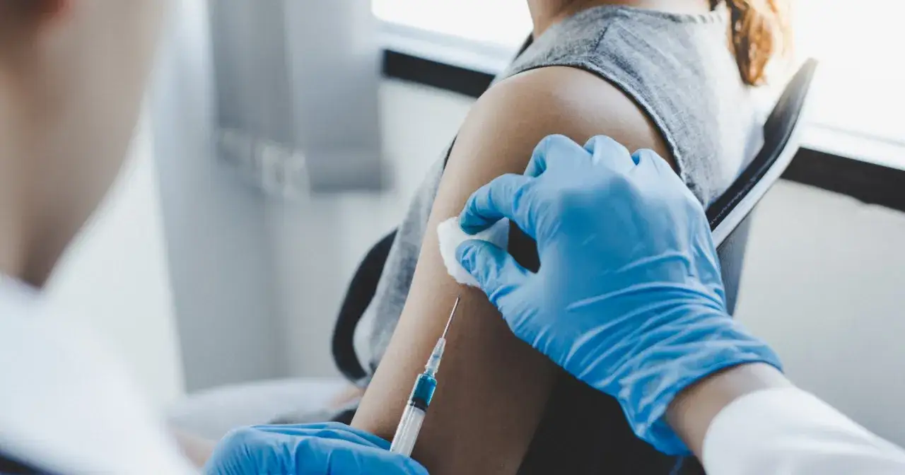 Osoba w niebieskich rękawiczkach podaje szczepionkę na HPV.