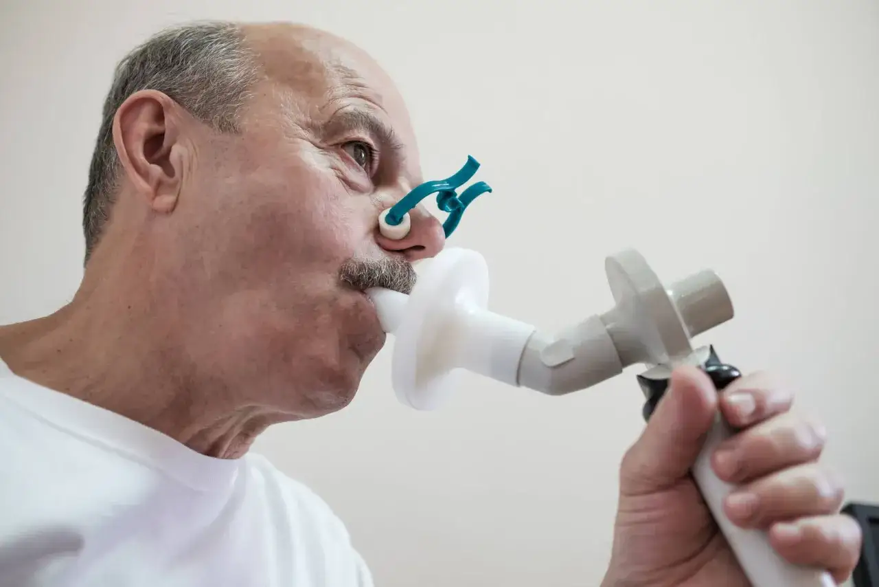 Starszy mężczyzna z klipsem na nosie wykonuje badanie spirometryczne. Wreszcie wyleczyłem się z POChP!