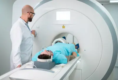 Pacjent leży w aparacie do rezonansu magnetycznego, przygotowując się do tomografii brzucha. Lekarz w białym fartuchu obsługuje panel sterowania.